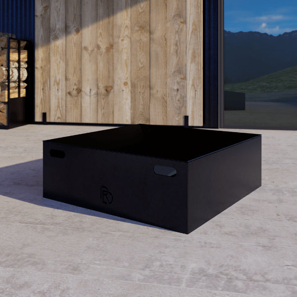 Box Firepit Standard – black rectangular outdoor fire pit with a wooden wall and mountain view in the background
