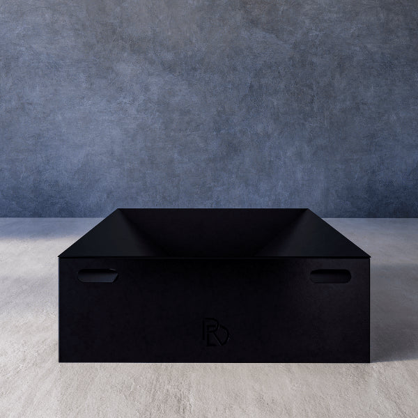 Box Firepit Standard – black rectangular firepit with a logo, placed on a gray surface with a blue gradient background